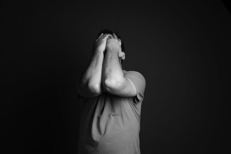 Persona cubriéndose el rostro con las manos, mostrando un gesto de desesperación o frustración relacionado con la ansiedad generalizada, en una imagen monocromática.